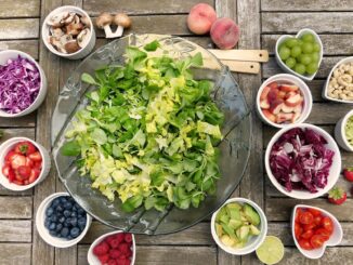 Eine Schüssel Salat mit verschiedenen Früchten und Gemüse auf einem Holztisch. Die gesunde Essensvariante ist perfekt für alle, die ihren Stoffwechsel ankurbeln möchten.