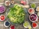 Eine Schüssel Salat mit verschiedenen Früchten und Gemüse auf einem Holztisch. Die gesunde Essensvariante ist perfekt für alle, die ihren Stoffwechsel ankurbeln möchten.